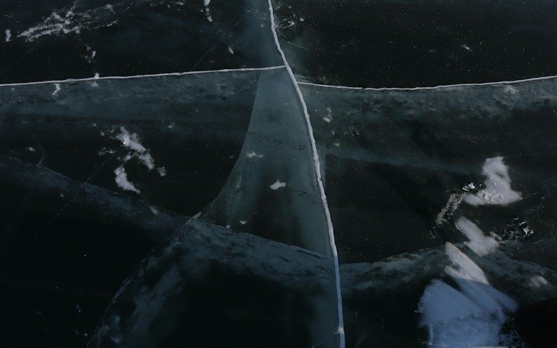 Clear black ice cut by a long crack, with patches of white snow ice lying on top (photo: Unsplash)