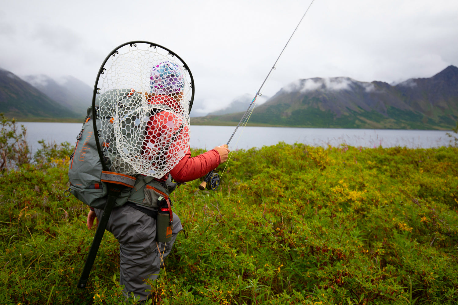 A fly angler with a Fishpond Nomad landing net slung on their back, working a river — the kind of buy-it-for-life gear this guide is built around