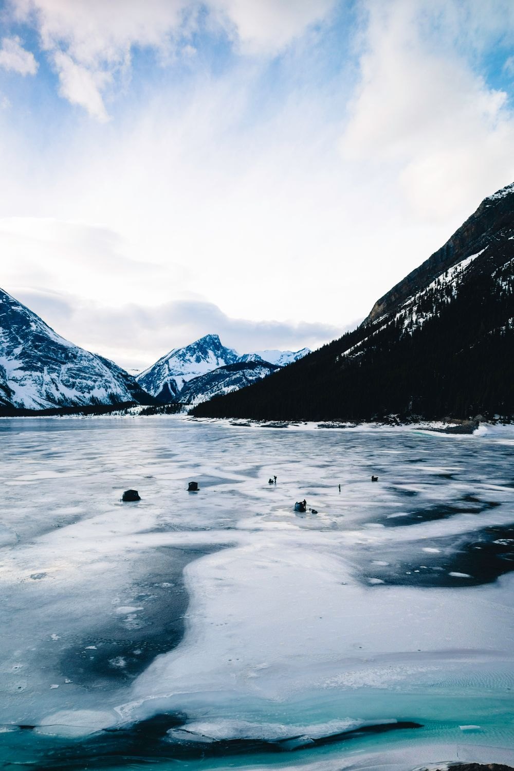 A vast frozen mountain reservoir under snow-capped peaks, a few anglers as specks on the ice (photo: Pexels)