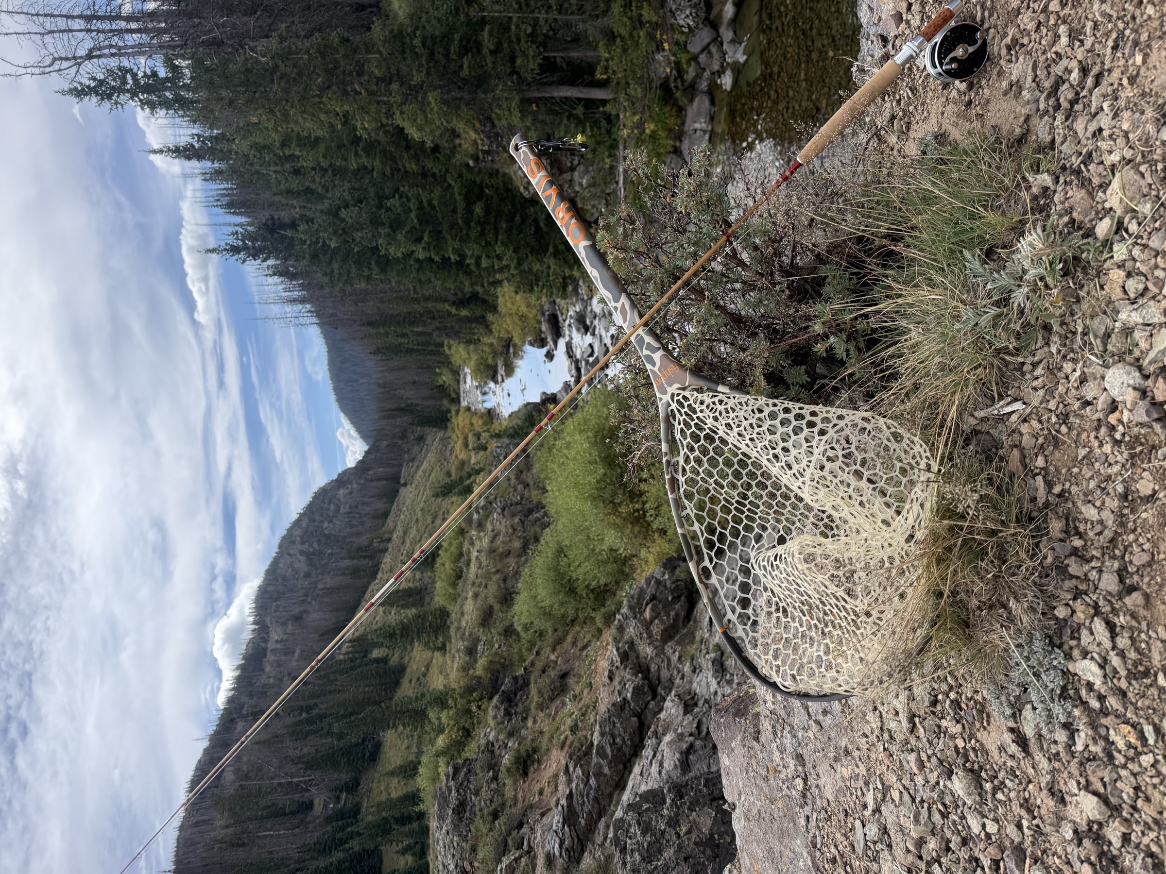 The Headwaters Madison at rest by a backcountry stream, a landing net hung on the blank