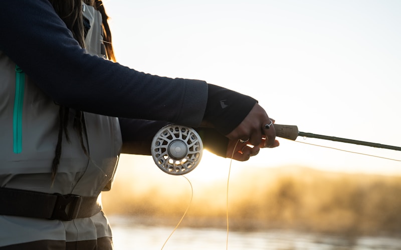 fly angler holding a fly rod with line out in golden evening light over a river