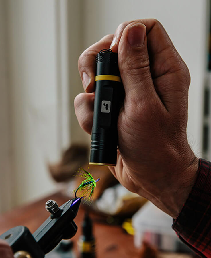 A tyer holds the Loon UV Bench Light just above a green flashy fly clamped in a tying vise, curing the resin on its head (photo: Loon Outdoors)