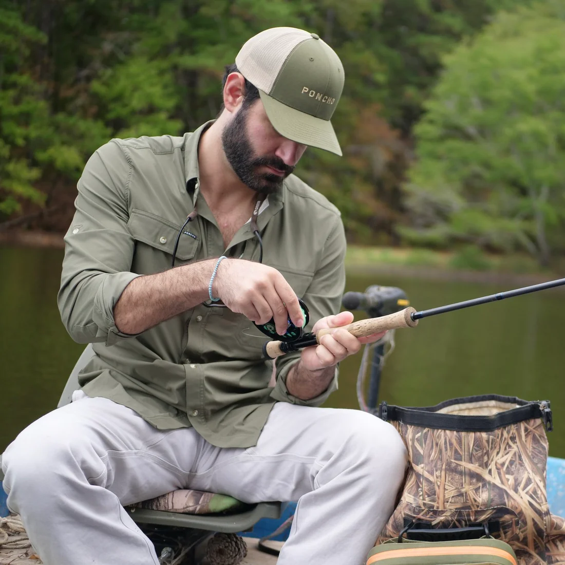 An angler in a moss-green Poncho Gunnison fishing shirt and Poncho cap, working a reel on the water (photo: Poncho)