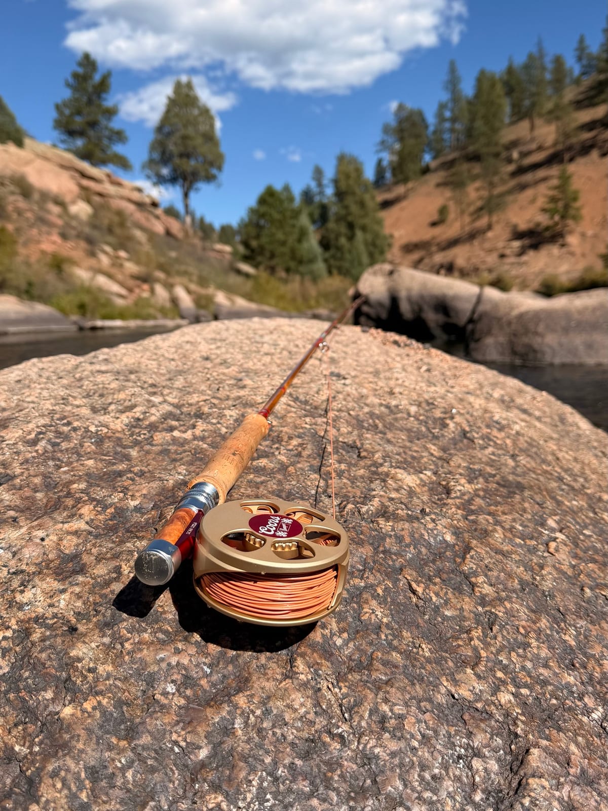 The Coors Banquet Cimarron Creek on my Headwaters Madison, laid across a granite boulder under a blue Colorado sky, pines and canyon walls behind.