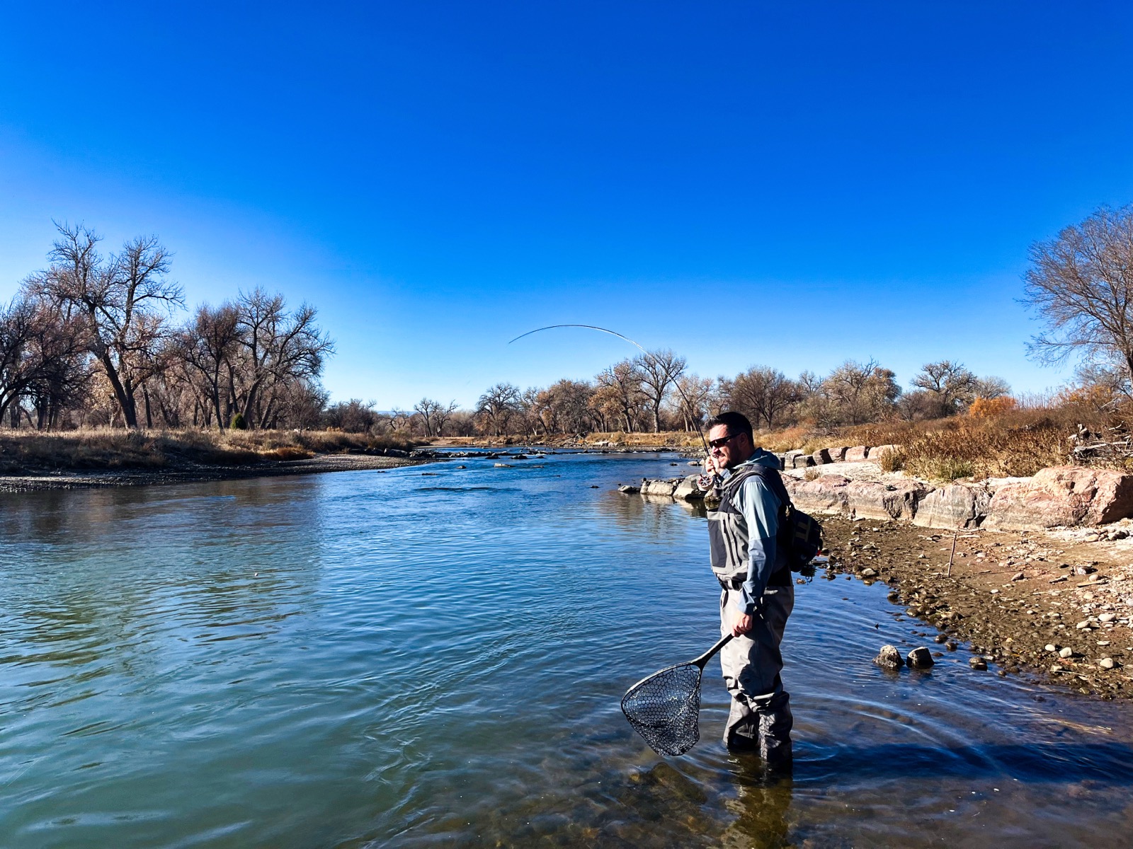 Knee-deep on a Colorado tailwater under a bluebird winter sky, my rod bent deep into a running fish with the net already in hand — the moment the reel's startup inertia either protects the tippet or pops it.